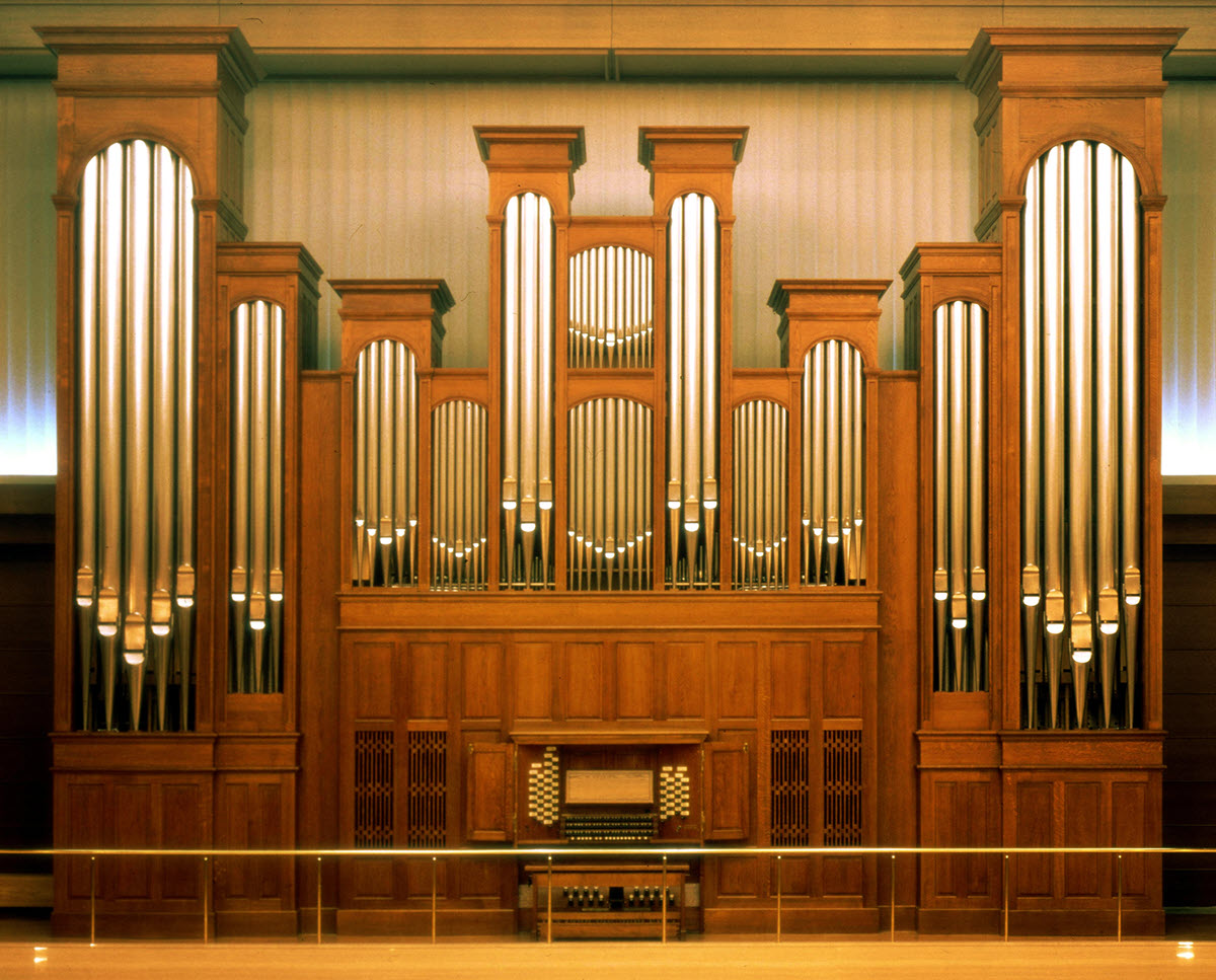 View of pipe organ with keyboard and full wall of pipes.