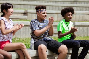 three students clapping while sitting outside 