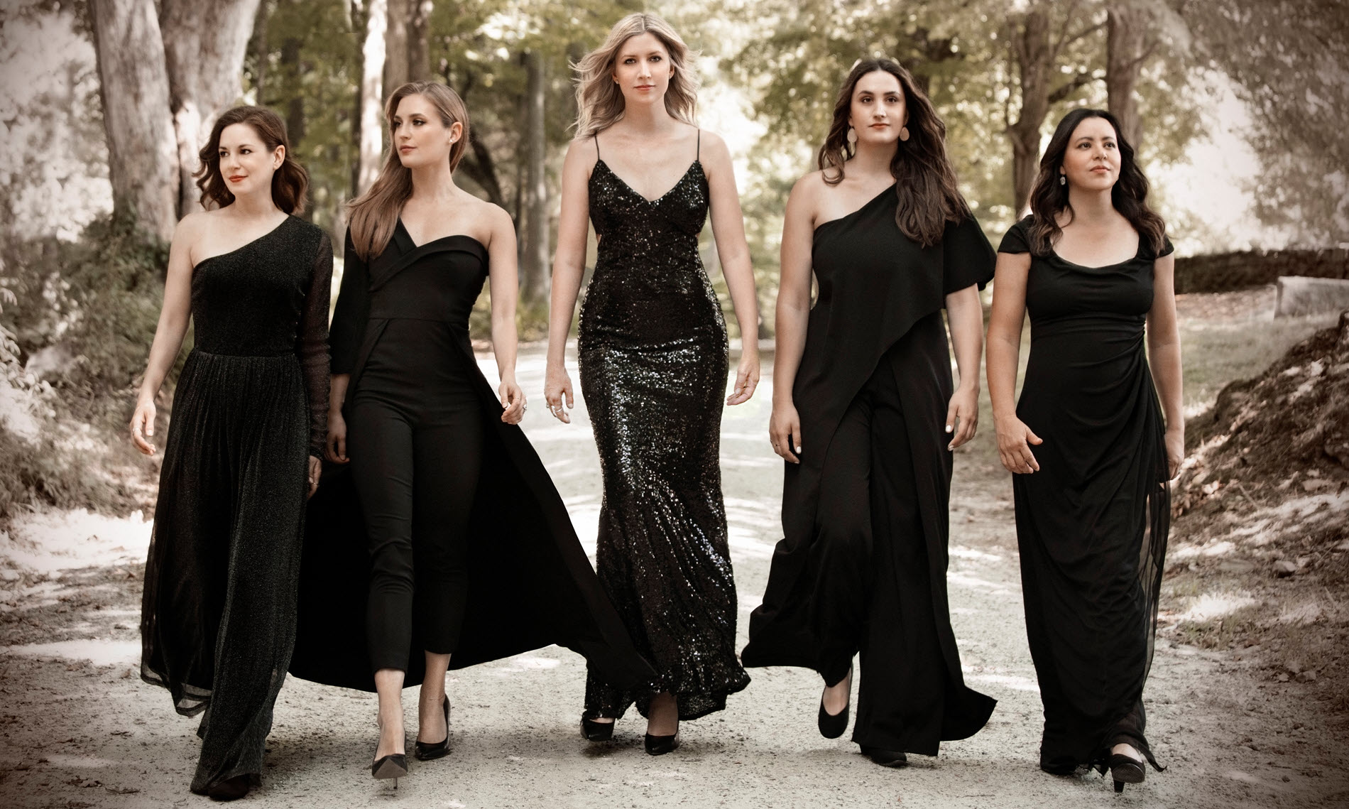 Five women in ballgowns walking down a path.