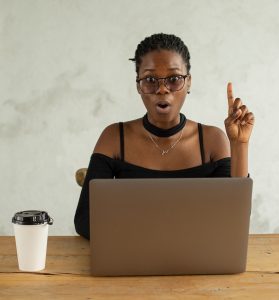 woman sitting in front of open laptop and holding index finger up