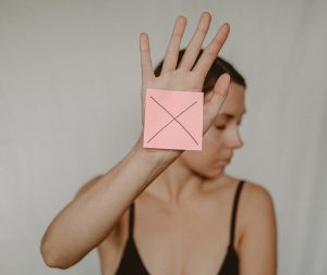 woman holding up her hand with a pink sticky note with a large X on it