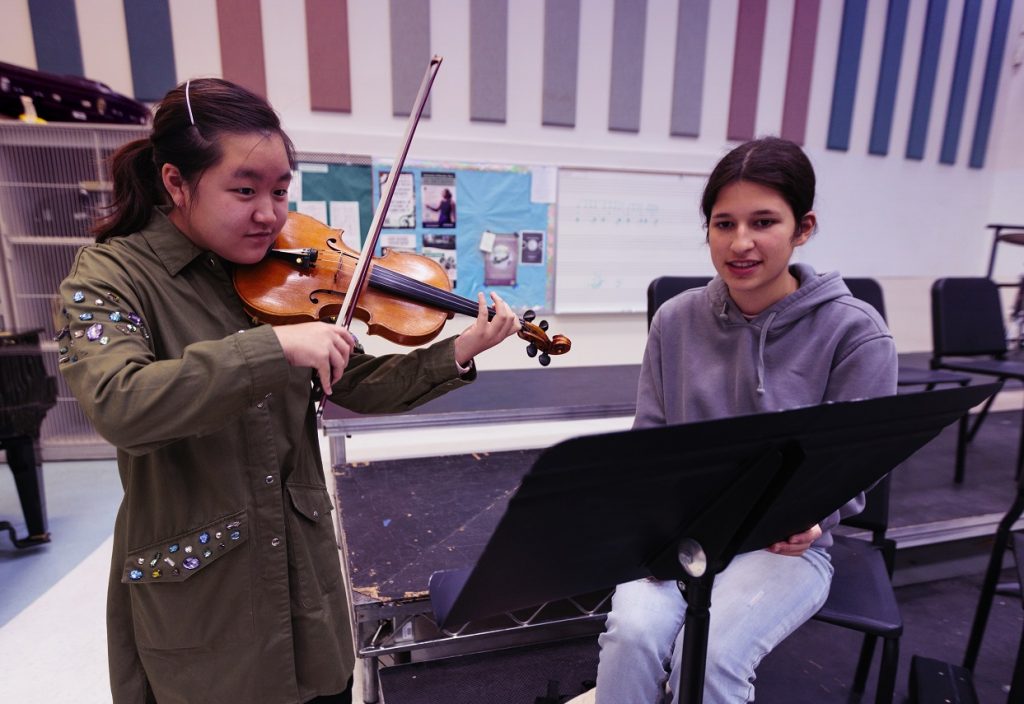 two female students in music class with one playing the violin