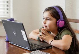 young girl sitting in front of open laptop and wearing headphones