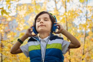 child with eyes clothes standing outdoors with headphones on
