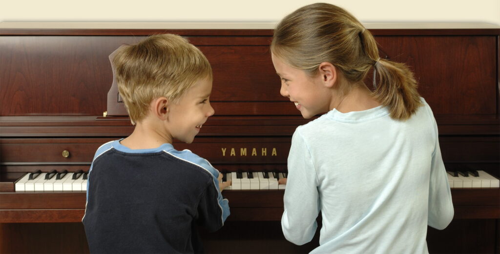 Two children at a piano smiling at one another.