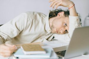 man sitting at desk in front of laptop and other papers slumped over and looking overwhelmed