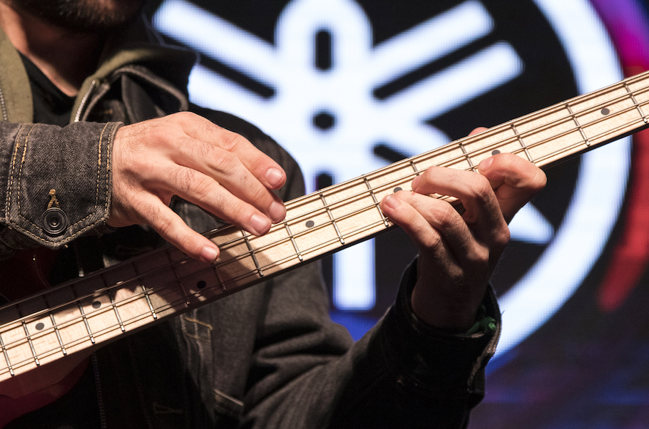 Closeup of someone playing bass guitar with a large Yamaha logo in background.