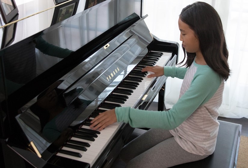 Young girl playing an upright piano.