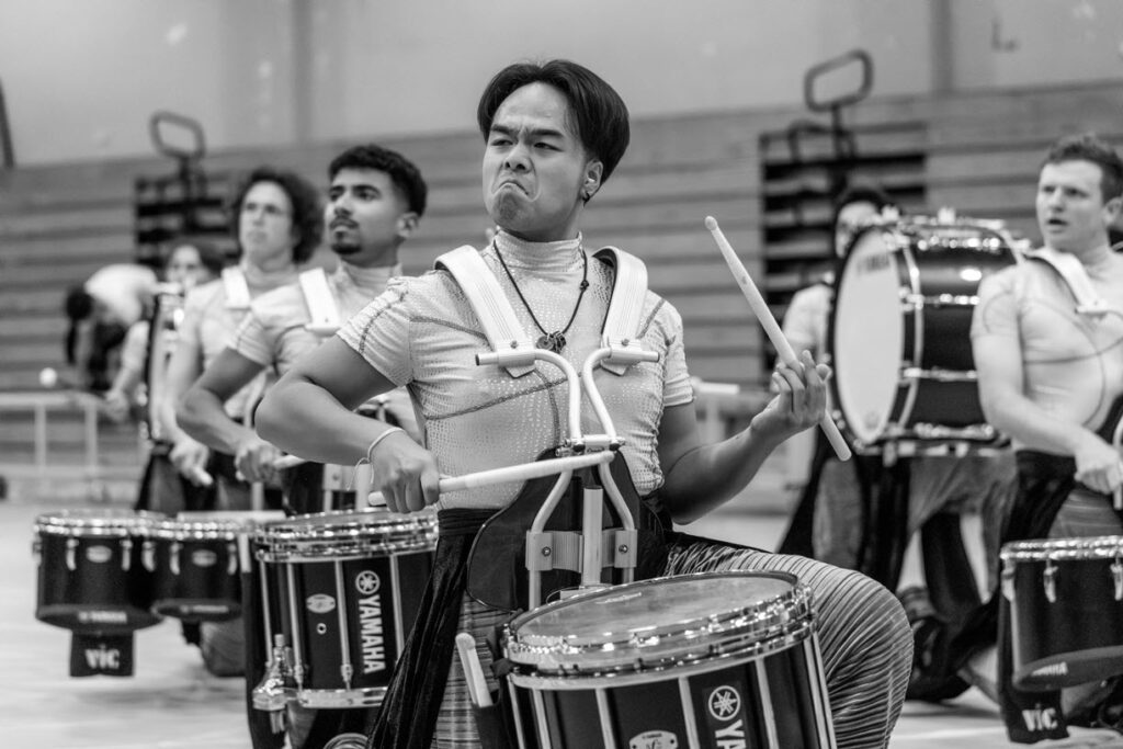 Closeup of snare drummers in a marching band performing in a gym.