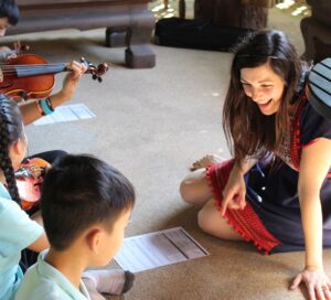 teacher sitting on ground and teaching music to group of Thai students