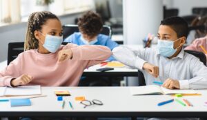 two students wearing masks and elbow bumping