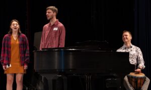 two student singing accompanied by music teacher on drums