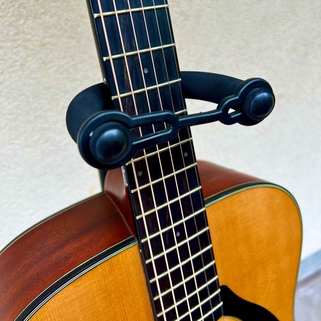 A guitar in a guitar stand with a rubber retainer holding it in place.