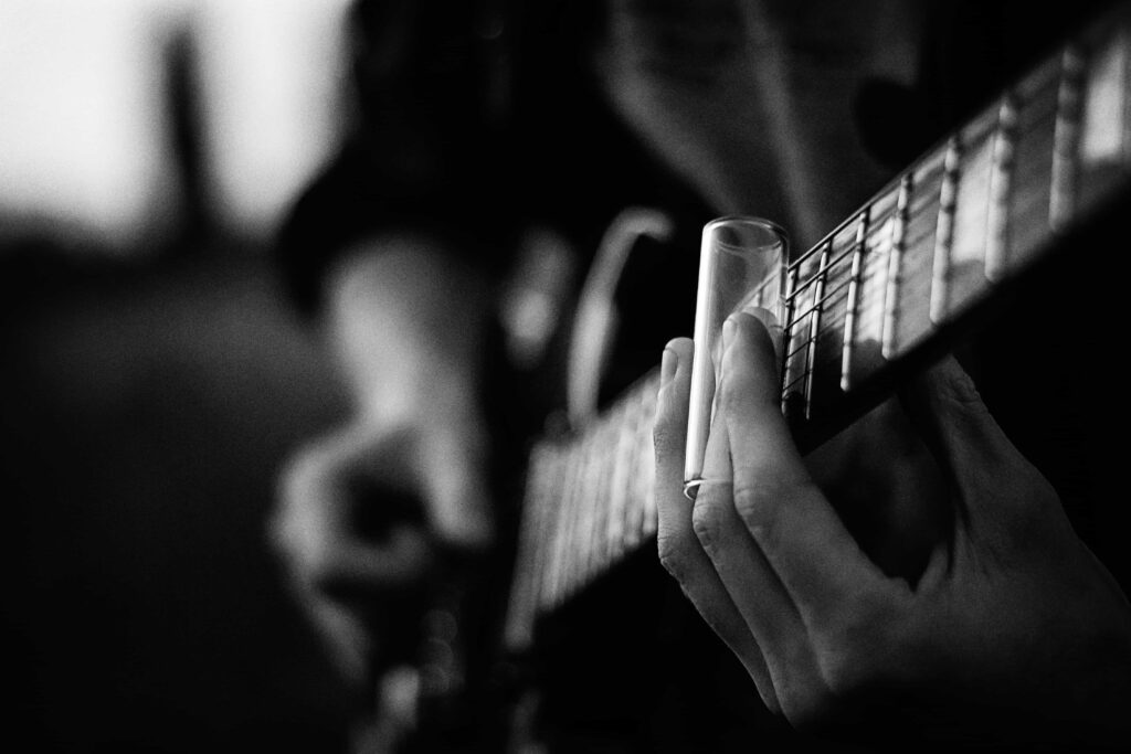 A black and white photo of an electric guitar being played with a slide.