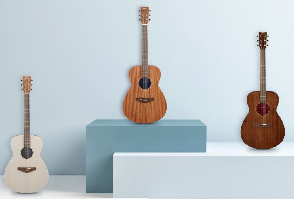 Three acoustic guitars, one white, one light brown, one dark brown.