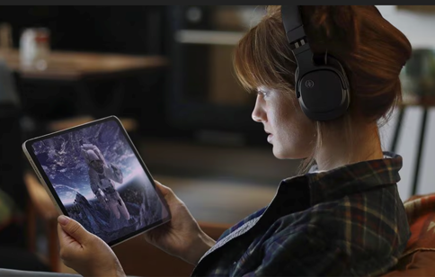 A young woman wearing headphones and watching a movie on her tablet.