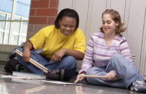 two percussion students looking at sheet music and holding drumsticks 