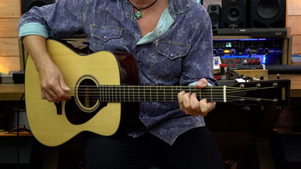 A man playing an acoustic guitar with medium brown sides.