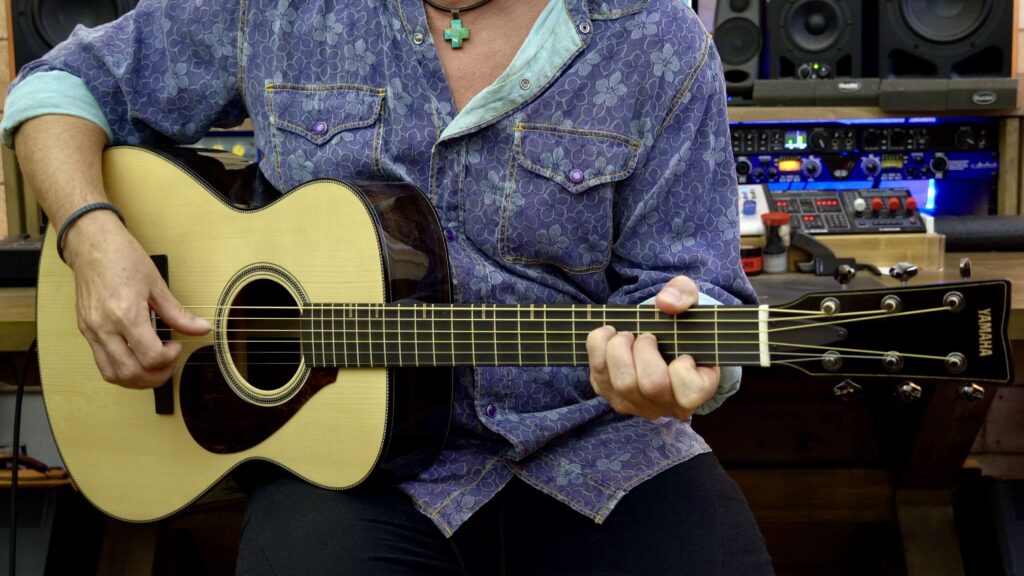 A man playing an acoustic guitar with dark brown sides.