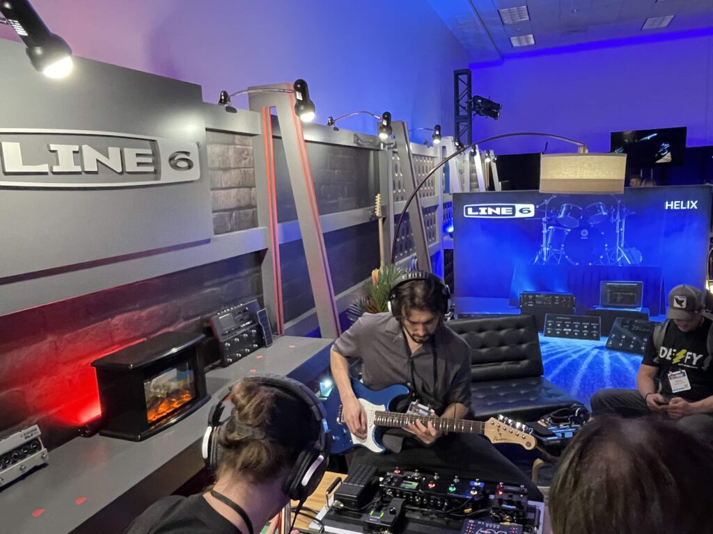 Two young men wearing headphones and playing electric guitars in a small room at 2025 NAMM.