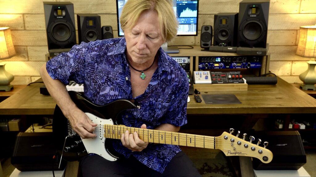 Man playing a solid-body black electric guitar with a maple fretboard.