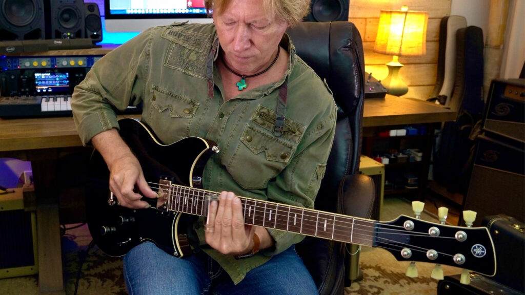 Man playing slide guitar on a chambered-body black electric guitar with a rosewood fretboard.