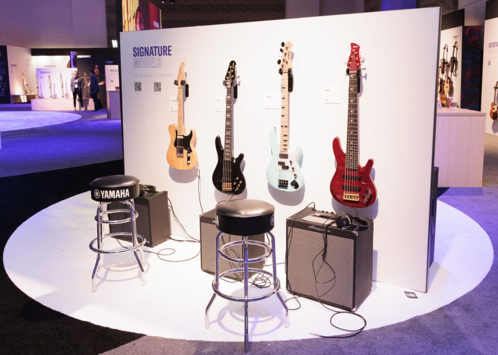 Four basses hanging on a wall display at 2025 NAMM.