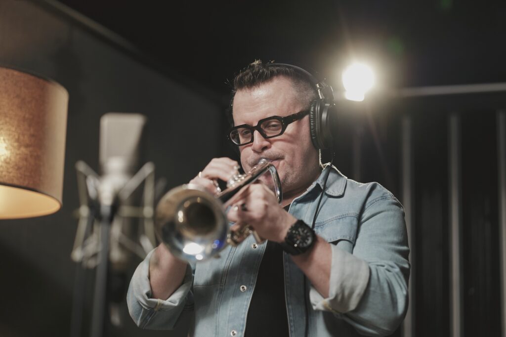 Hero image, man in blue shirt playing trumpet.