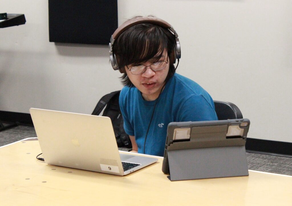 student wearing headphones and sitting at desk with a laptop and tablet