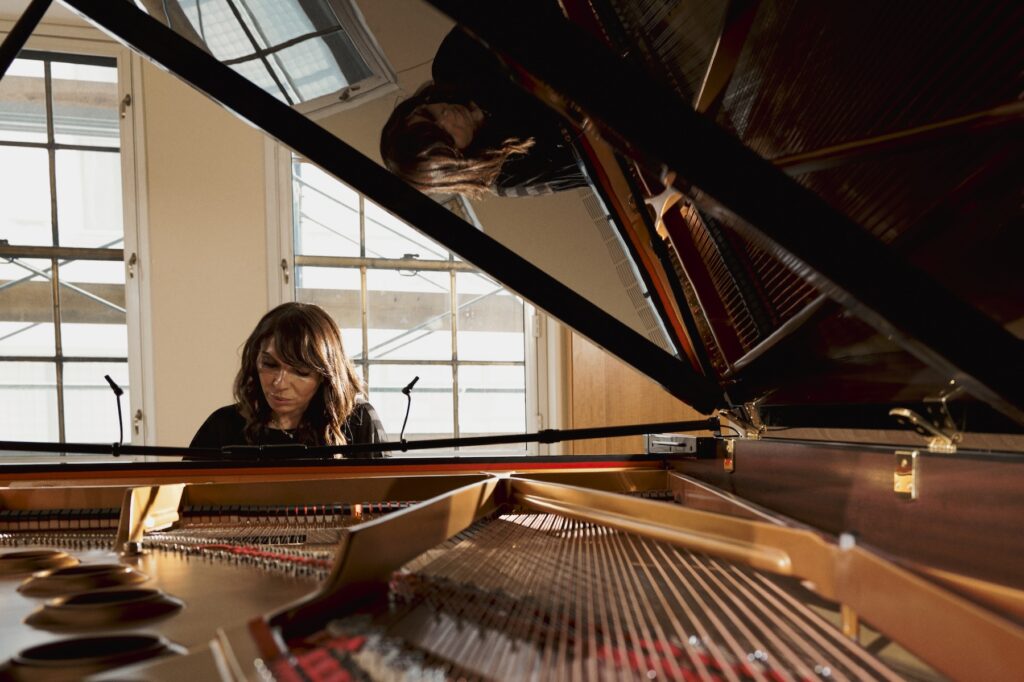 Close up version of image of woman sitting at a grand piano, playing music with the piano lid open.
