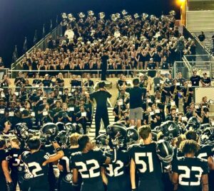 marching band performing in stands while football players cheer from the field