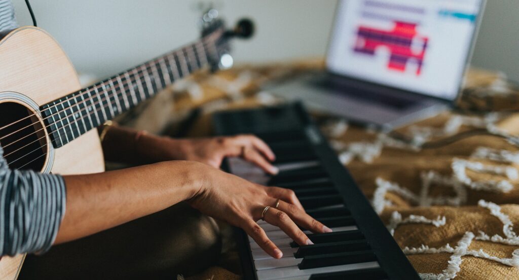 someone holding guitar and playing keyboard with laptop
