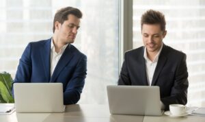two men working on laptops and one of them is peeking at the other's screen