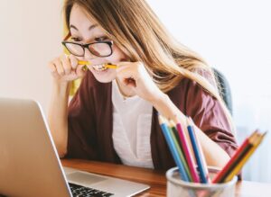 stressed woman biting on pencil while looking at laptop