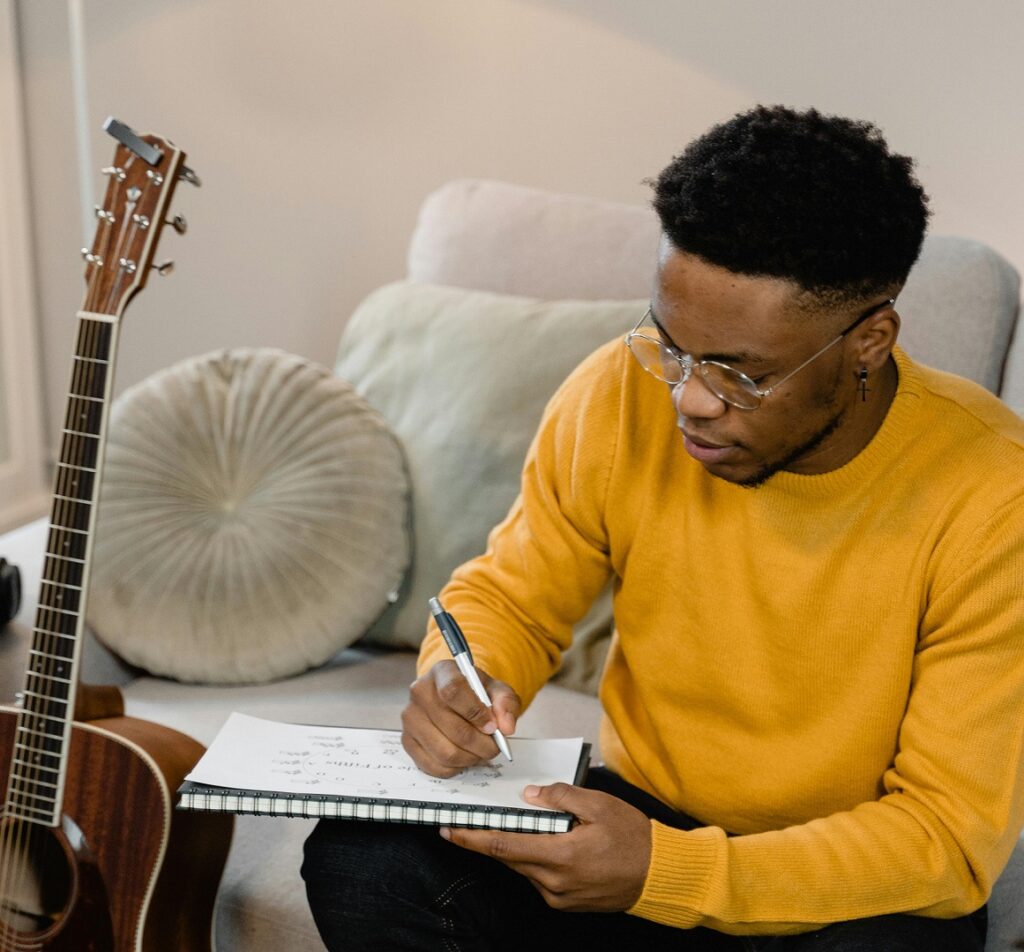 man writing song with guitar on stand next to him