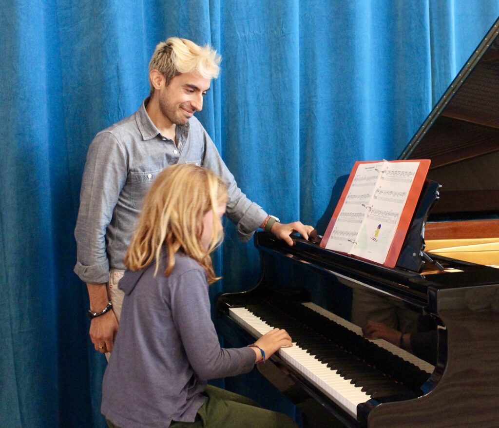 female student playing piano with one hand while instructor watches