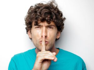 man holding index finger to his lips, indicating "be quiet"