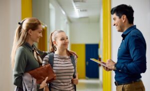 teacher speaking to parent and student in school hallway 
