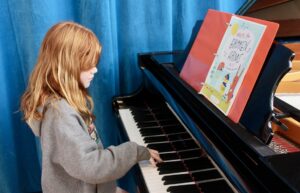 female student playing piano with one hand