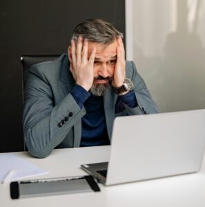 man sitting at desk in front of laptop with his hands on his face