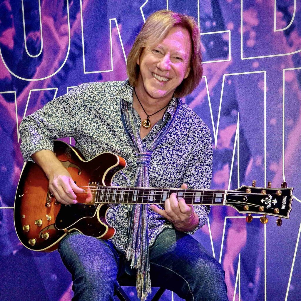 A smiling man playing a Yamaha SA2200 semi-hollowbody electric guitar with a sunburst finish.