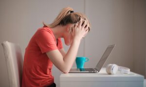 frustrated woman sitting in front of laptop with head in her hands
