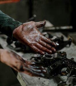 greasy hands held up over engine parts 