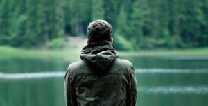 man sitting outdoors looking onto lake