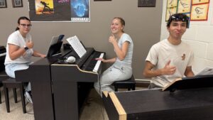 students in piano class holding their thumbs up