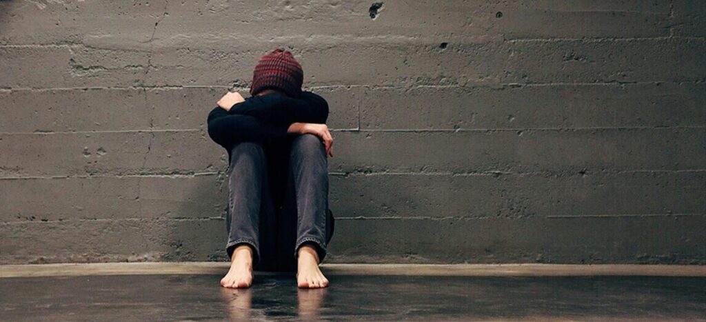grieving student sitting on ground with head in his arms