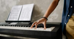 student standing next to keyboard and playing a chord with one hand 