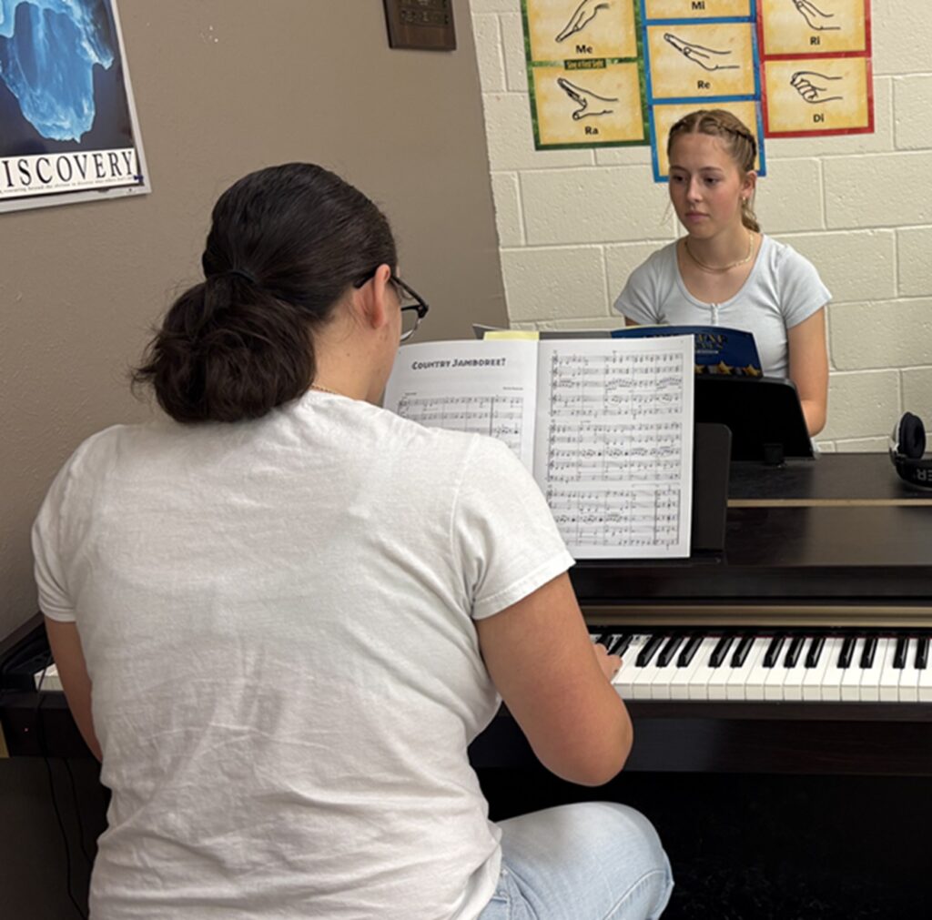 two students playing piano in music class
