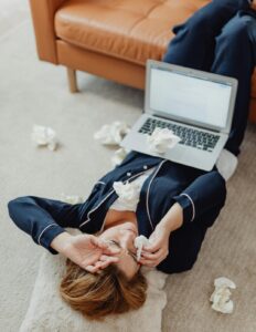 upset woman laying on the ground with laptop on her stomach and tissue papers strewn around her 