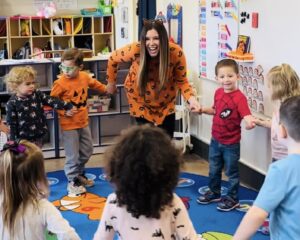 Dr. Cassandra Eisenreich holding hands and walking in a circle with preschoolers during Halloween class